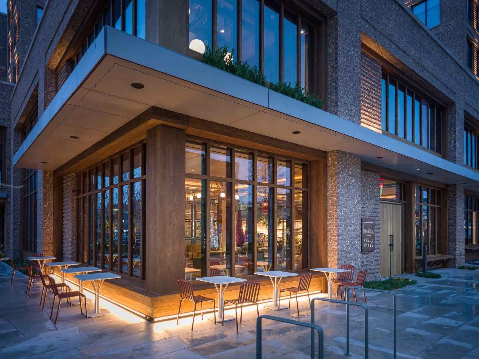 The Compton at dusk, glass-fronted ground floor lit up, sidewalk seating on the Bentonville square
